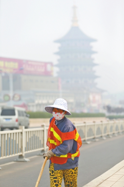 近日，在古都洛陽，環(huán)衛(wèi)工人身后的“天堂”被霧霾籠罩著。