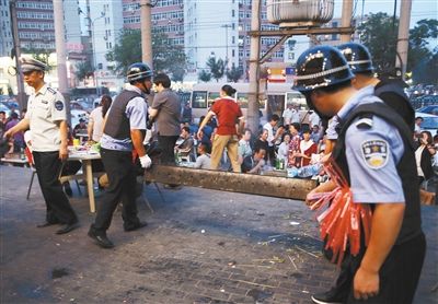 6月13日晚8點，朝陽路和青年路交叉口西側(cè)，一次聯(lián)合執(zhí)法行動中，輔警與協(xié)管抬走商戶的燒烤用具。新京報記者 尹亞飛 攝