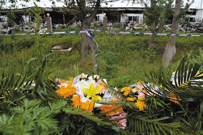 昨日，吉林省德惠市吉林寶源豐禽業(yè)有限公司燃燒事故現(xiàn)場(chǎng)警戒線外，遇難者家屬在路邊擺放了花圈祭奠逝去的親人。吳江 攝