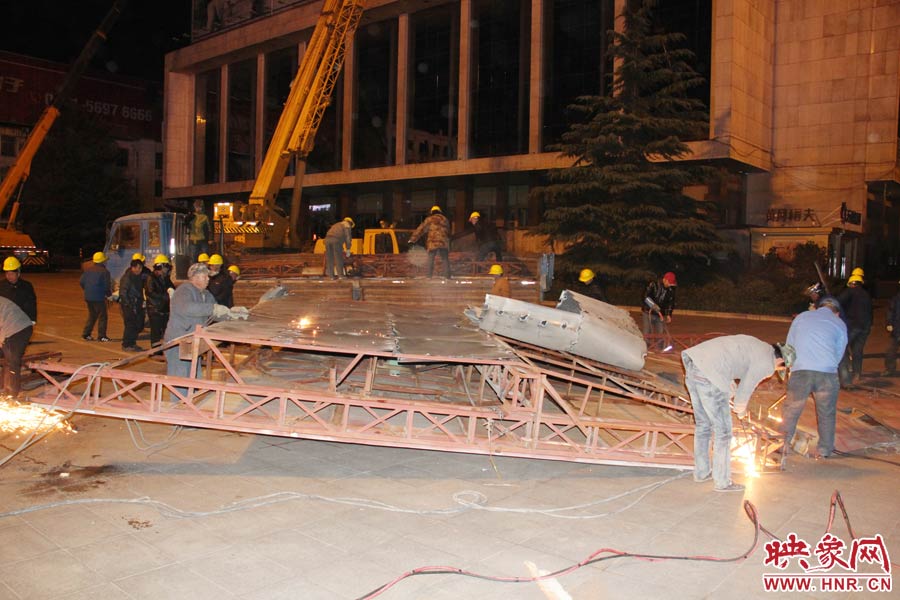 地面上的20多名工人對(duì)吊裝下的廣告牌進(jìn)行分割。