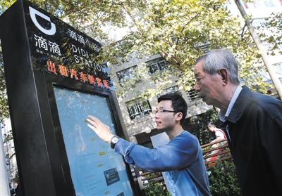 10月15日，滴滴工作人員（左）指導(dǎo)乘客使用“滴滴車站”的電子屏預(yù)約出租車。