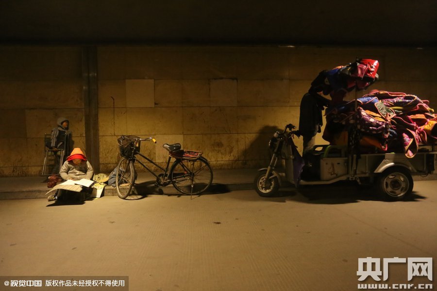 2015年11月8日晚，鄭州，7歲男孩涵洞橋下陪父母練攤，路邊燈下坐小馬扎上寫作業(yè)。