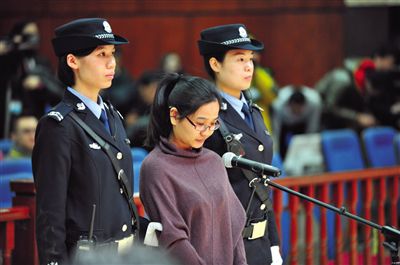 被告人盧梅低著頭，站在朝陽法院刑事審判庭的被告席上。