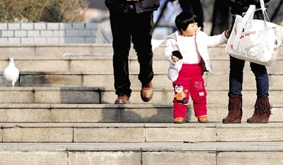 昨天中午，一女孩拉著家長(zhǎng)的手在紫荊山公園曬太陽(yáng)，氣溫升高，孩子的棉衣解開(kāi)了扣子。