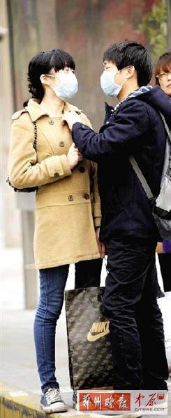 公交站臺(tái)上，一對(duì)年輕人戴著口罩，系緊衣領(lǐng)。